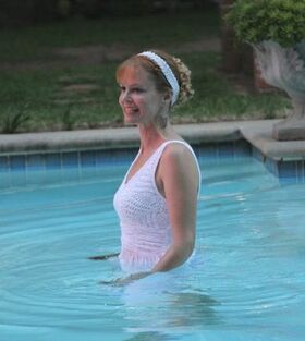 Smiling blonde woman in white dress standing up to waist in a pool.